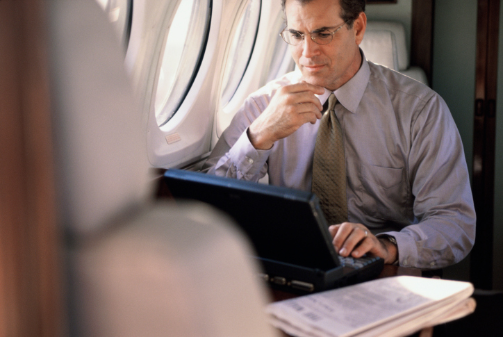 business man on private jet doing work on laptop sitting next to window