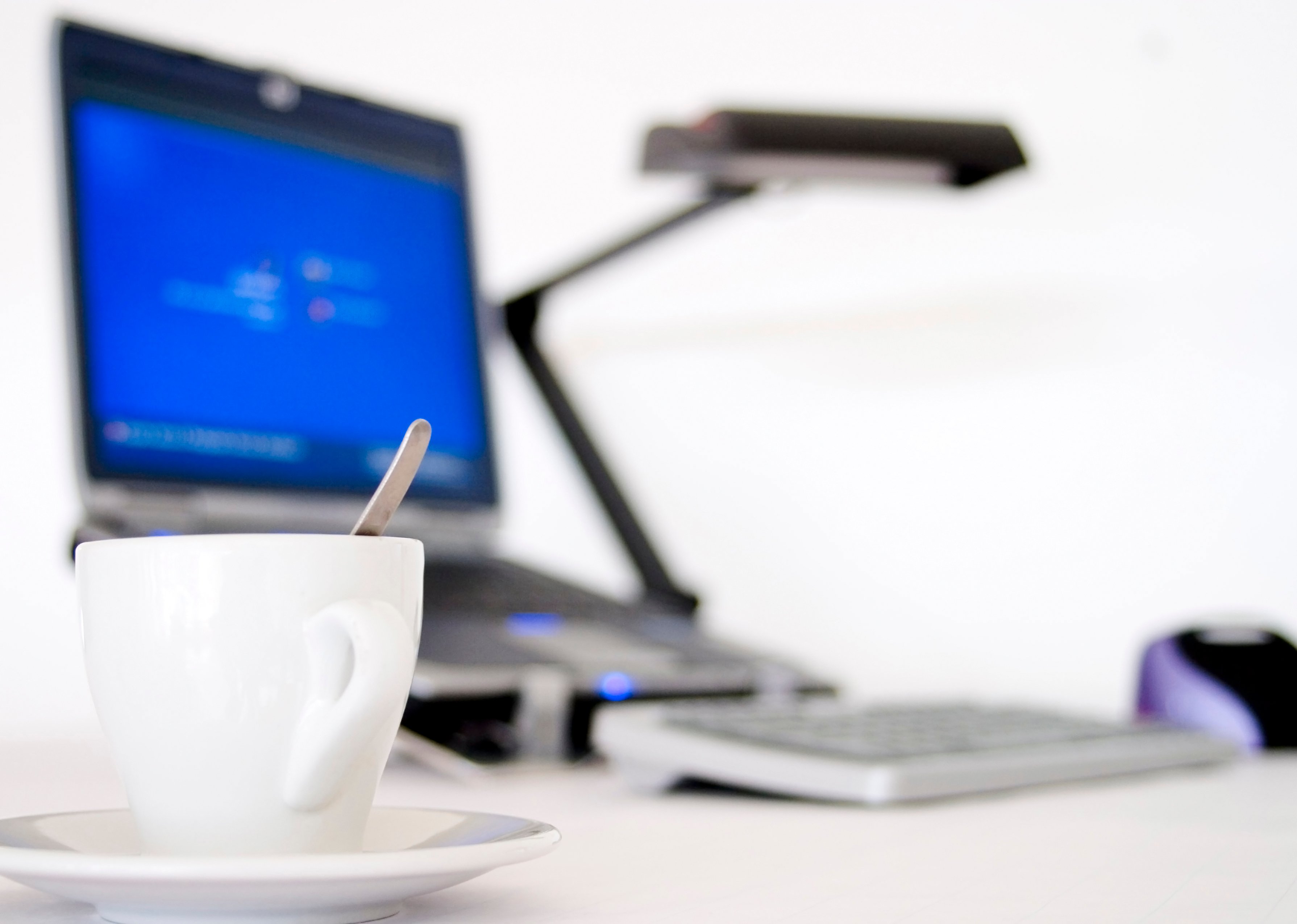 image focused on cup of coffee, with blurry laptop in background