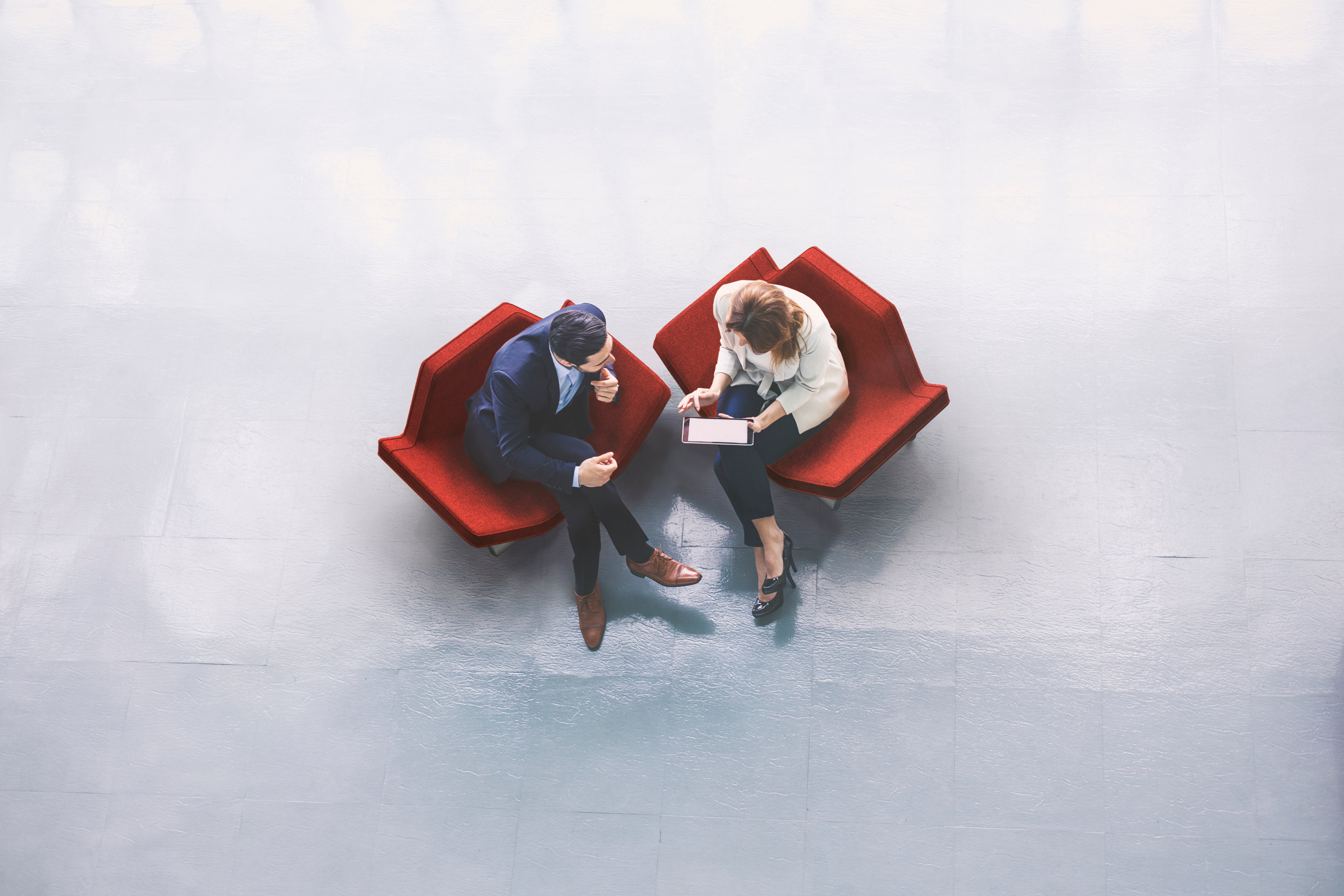 birds-eye-view of two coworkers sitting in modern red chairs discussing business