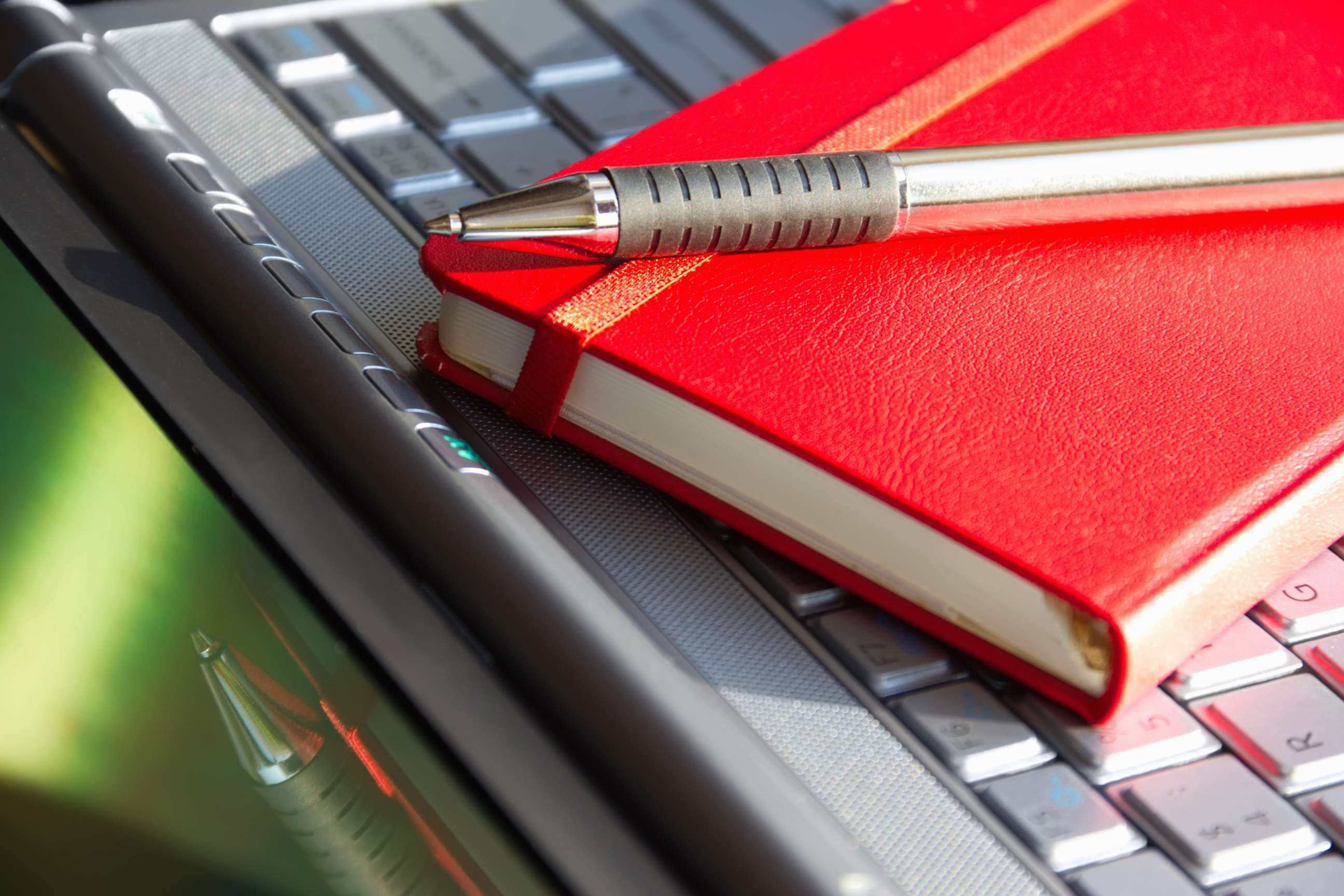 red notebook with pen on top of keyboard