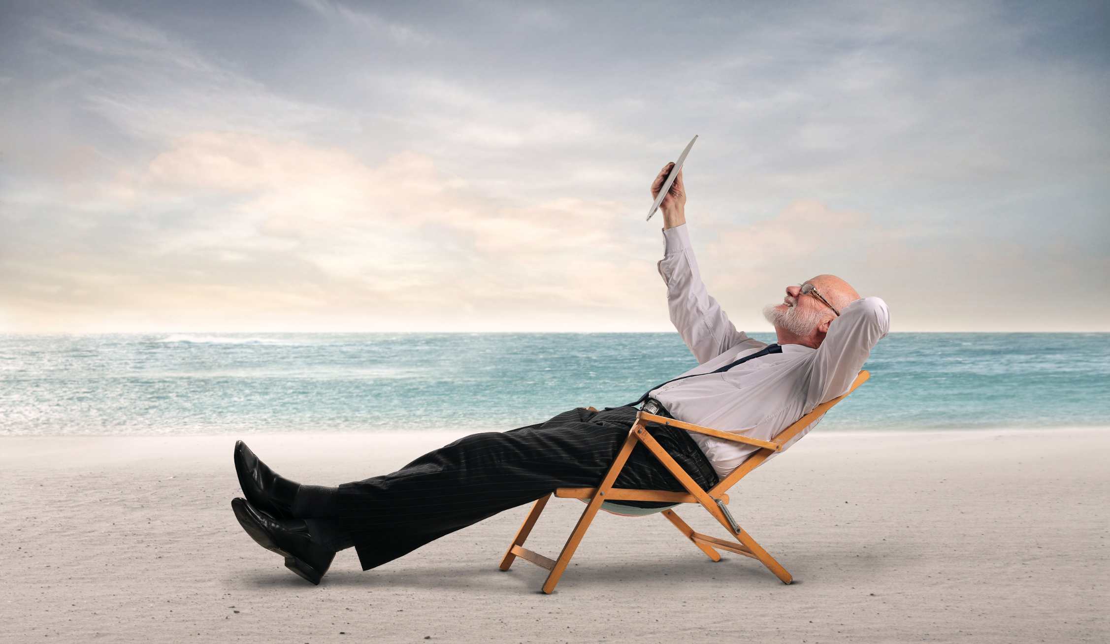 business man relaxing on beach holding tablet