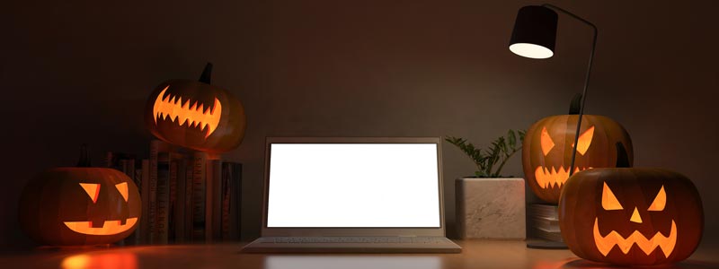4 carved pumpkins around a laptop in the dark w one light 
