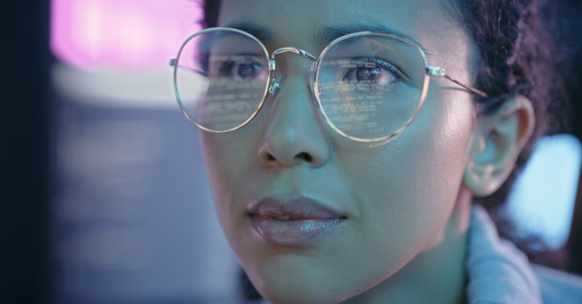 Closeup of a woman wearing glasses with screen reflections on the lenses.