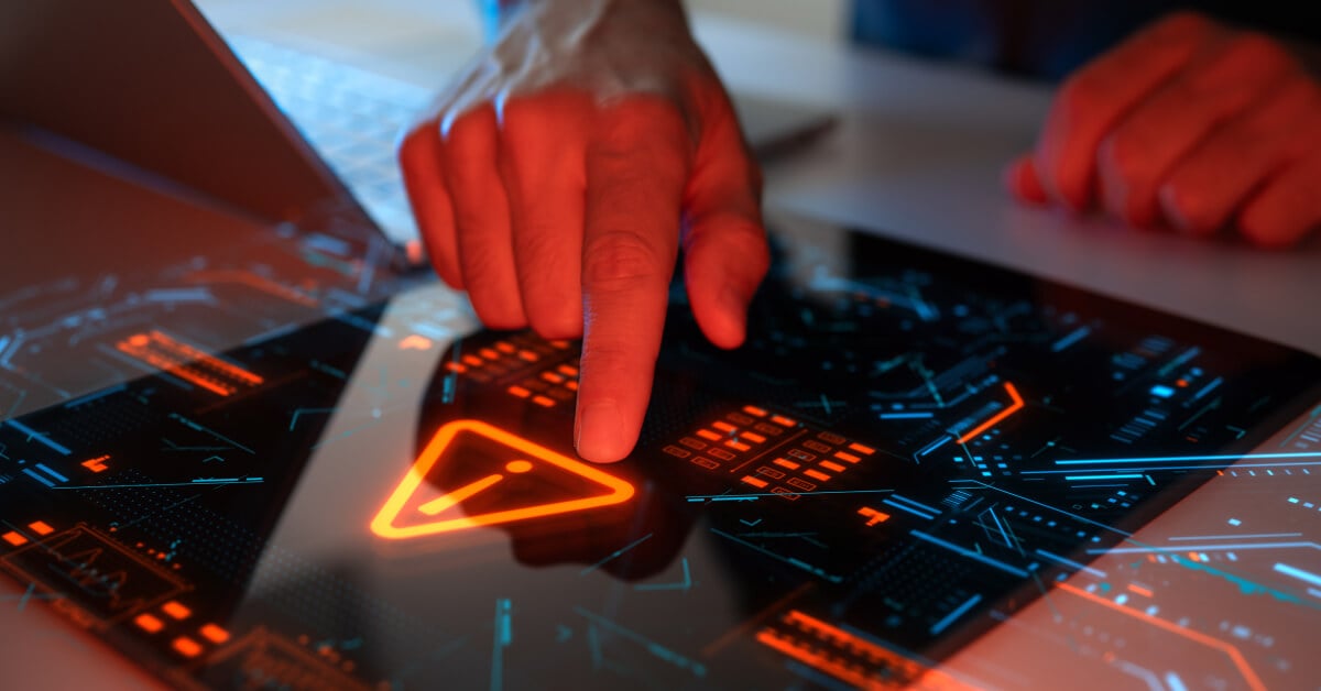 Person's index finger pressing a glowing warning triangle symbol on a futuristic touchscreen interface, with red and blue digital graphics suggesting a cybersecurity alert or system warning.