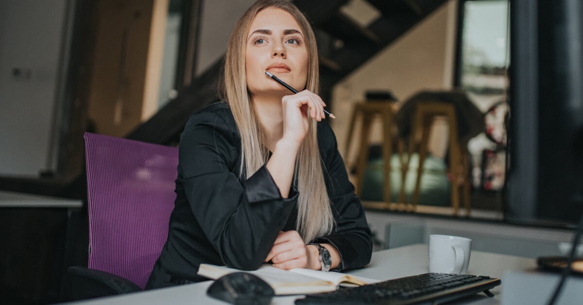 Woman sitting at a work desk looking of into the distance.