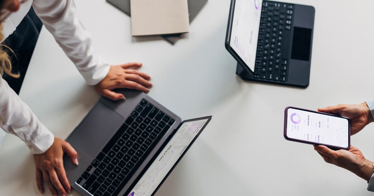 Overhead shot of one person interacting with a laptop, and another interacting with a smartphone.
