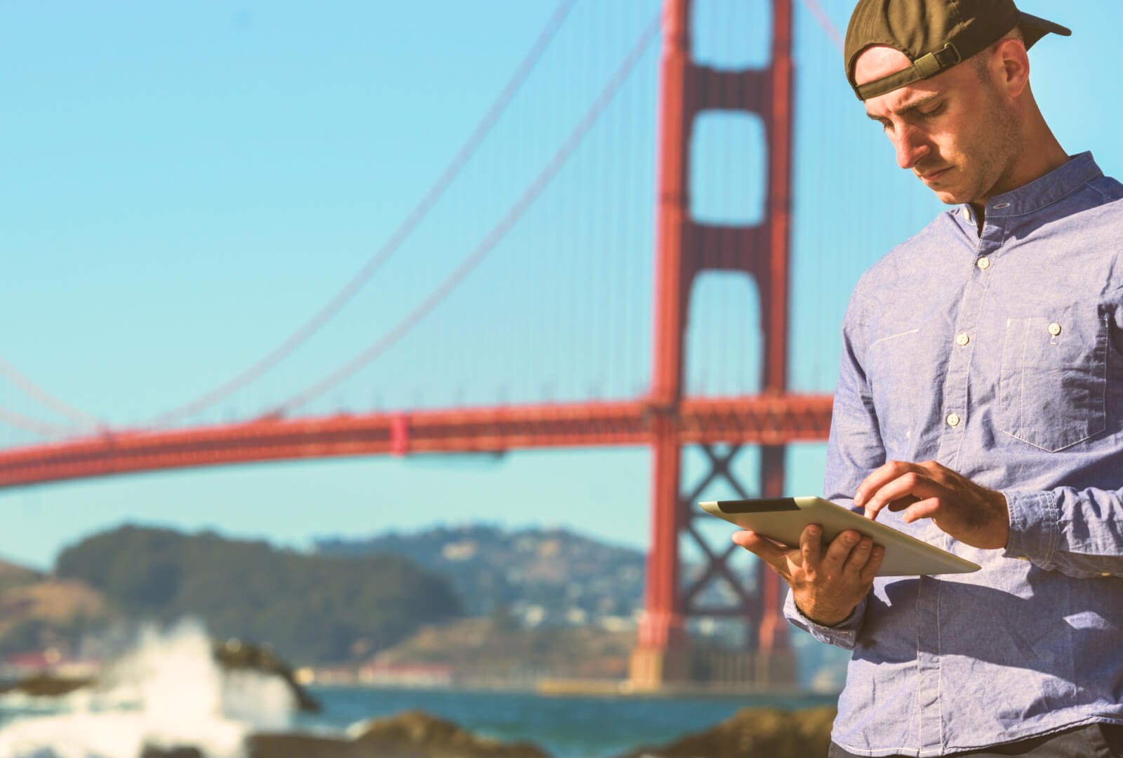 Man interacting on a smartphone outside with the golden gate bridge in the background.