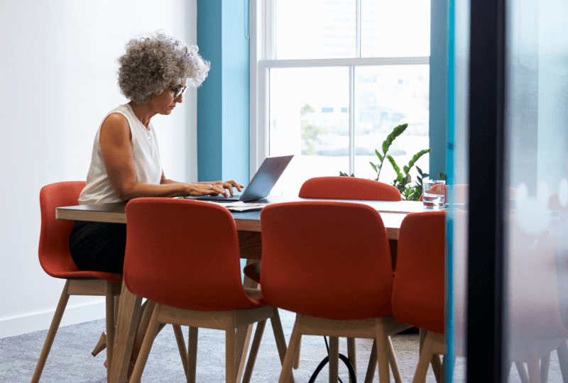 Woman working on a laptop at a dining table.
