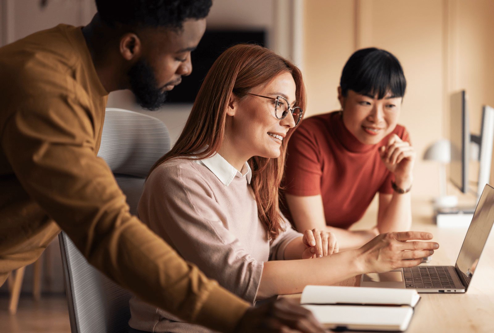 Three people interacting with a laptop on a desk.