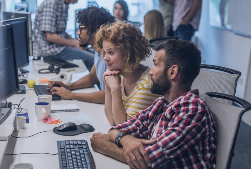 A group of people in an office interacting with their desktop computers.
