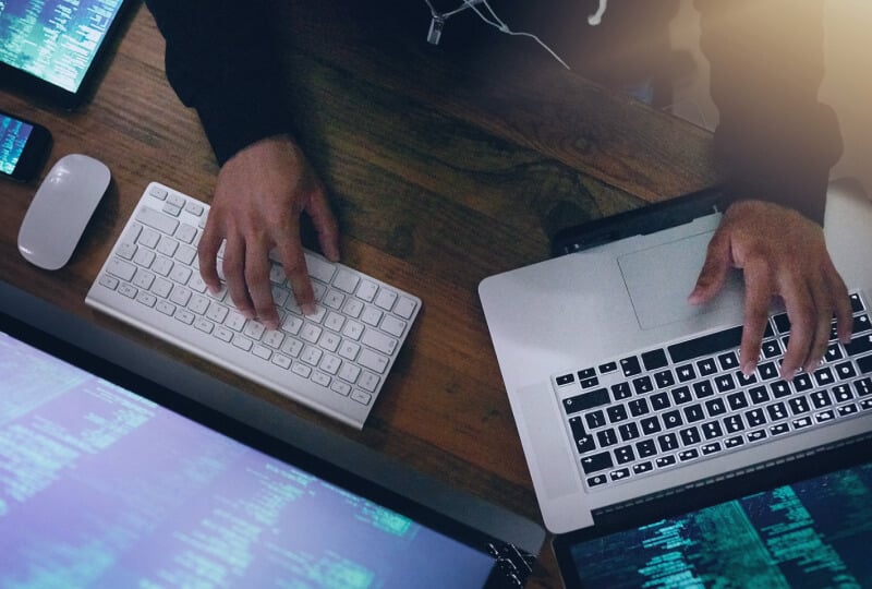 Overhead shot of a person interacting with a laptop keyboard with their left hand, and a desktop keyboard with their right hand.