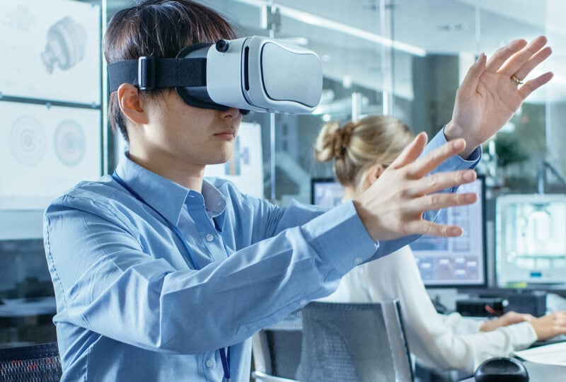 Man wearing a VR headset in an office with his arms outstretched as if he's interacting with something displayed in the headset.