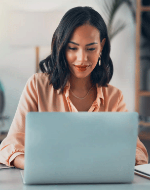Smiling woman sat behind a desk interacting with a laptop.