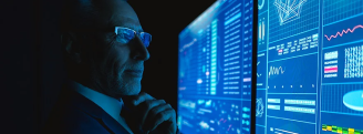 A man standing in a dark room, looking thoughtfully at large screens displaying various data visualizations, graphs, and charts with a blue color theme. The person is wearing a suit and has their hand on their chin, suggesting analysis or monitoring of information.