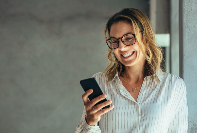 Smiling woman standing in a brightly lit office interacting with her smartphone.