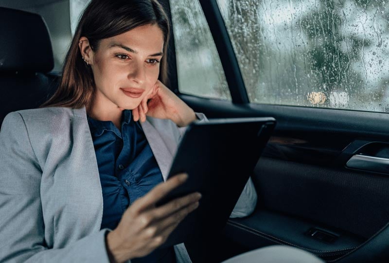 a woman looking at a tablet device in the back of a car