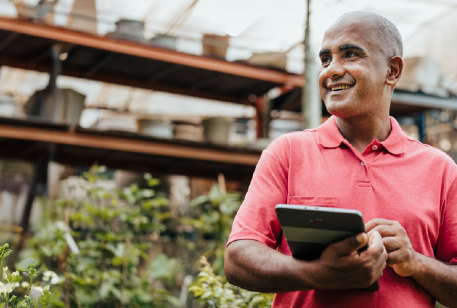 Man holding a tablet computer in a brightly lit garden warehouse.