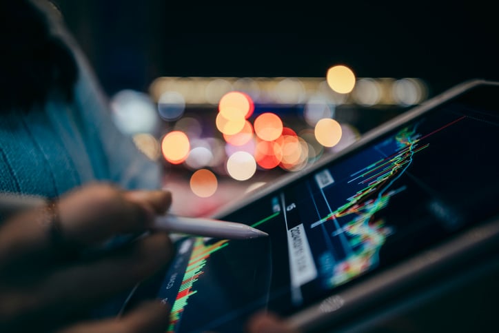 Close-up of a person using a stylus on a tablet displaying financial charts