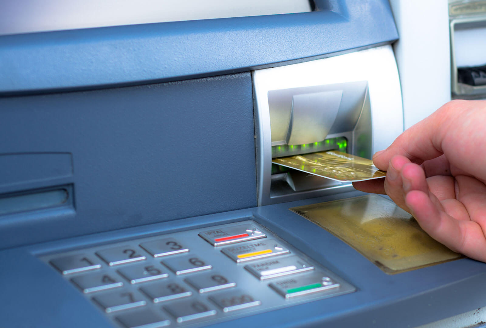 Hand inserting a debit card into an ATM.
