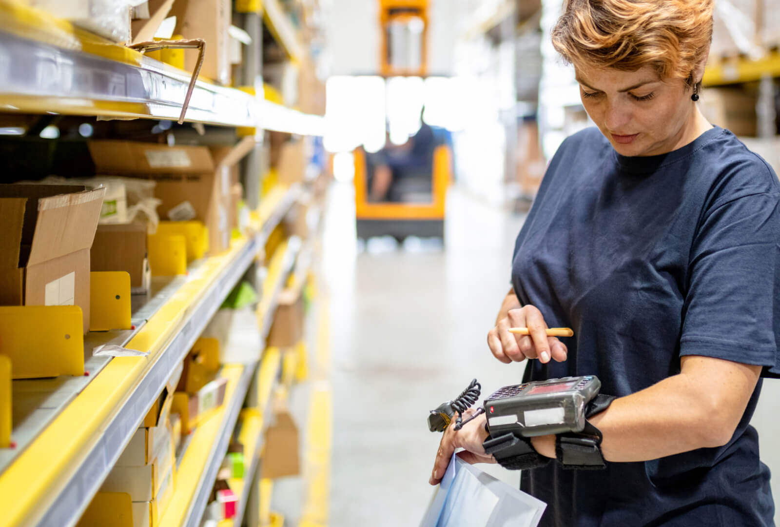 Woman in a warehouse interacting with a mobile device attached to her wrist.