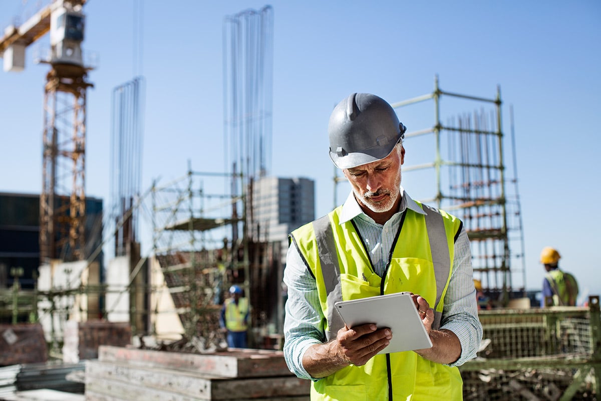 Construction worker in a hard hat and high-visibility vest holding a tablet at a construction site