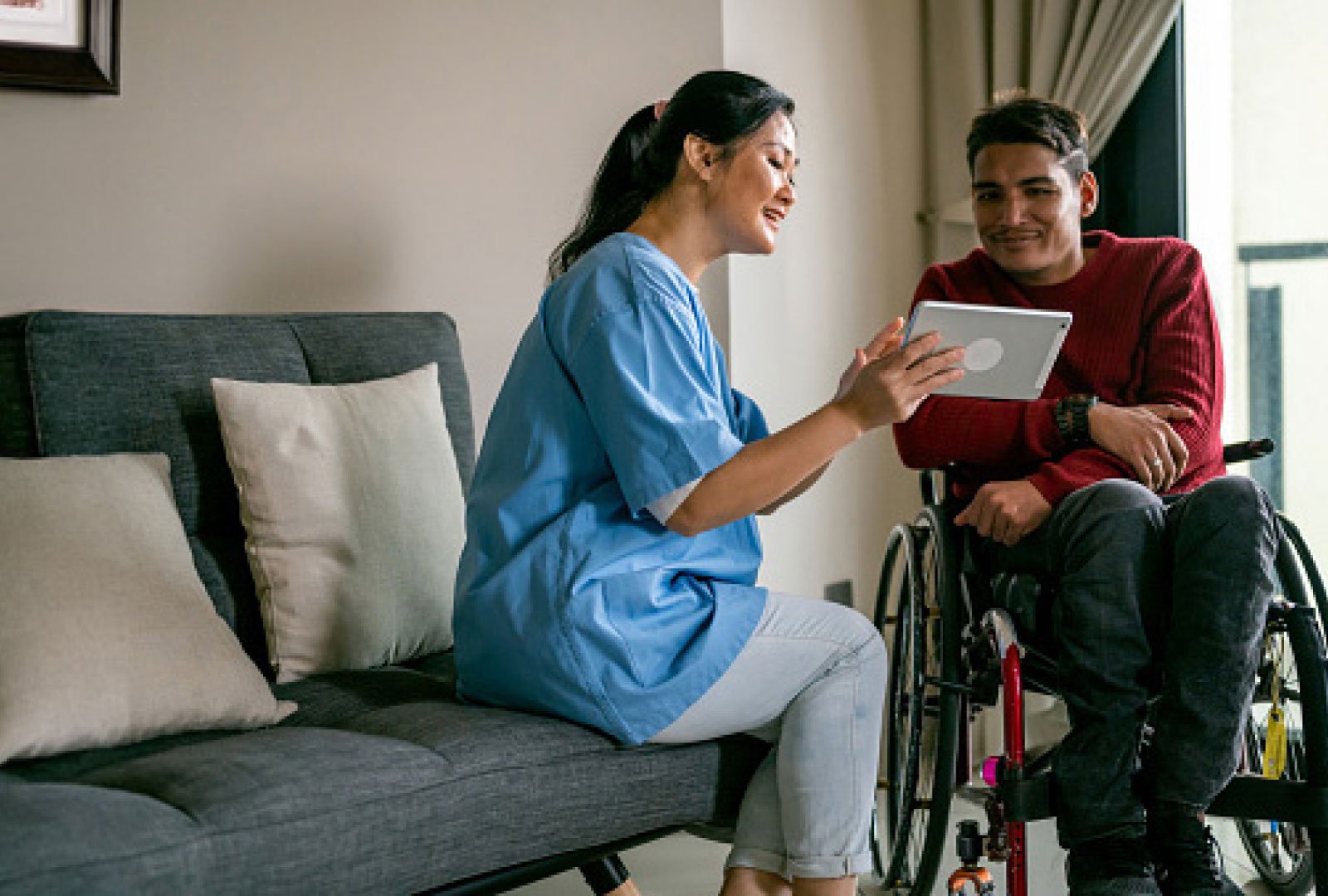 Nurse holding a tablet device in front of a smiling man in a wheelchair.