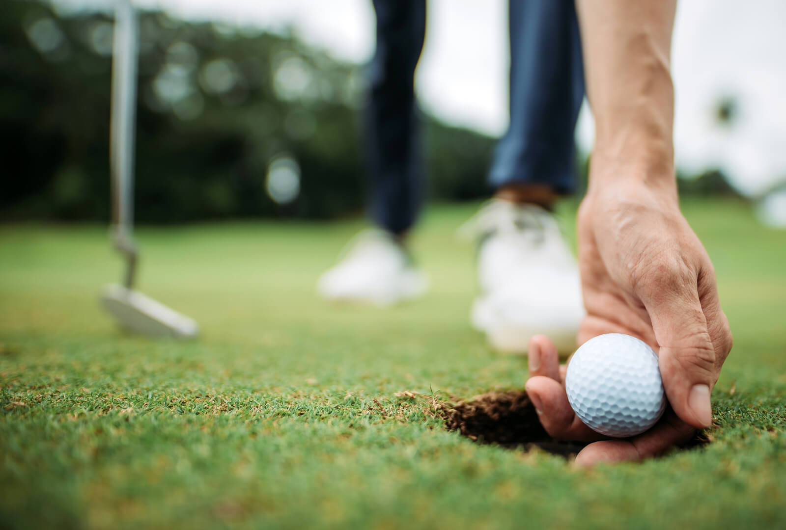 A man's hand removing a golf ball from the hole it was hit into.