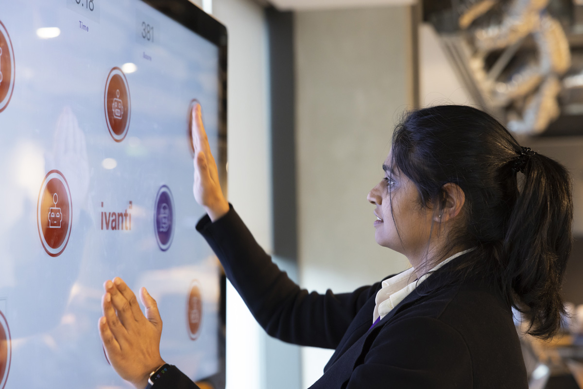 A woman interacts with a large touchscreen displaying the Ivanti logo and several icons