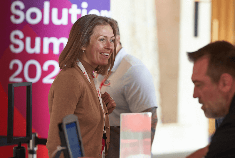 A woman standing near a Ivanti Solutions Summit poster smiling.
