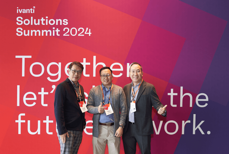 Three smiling men standing in front of a Ivanti Solutions Summit wall.