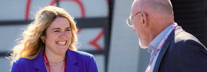 eine lächelnde blonde Frau im Gespräch mit einem glatzköpfigen Mann