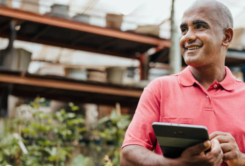 Man holding a tablet computer in a brightly lit garden warehouse.