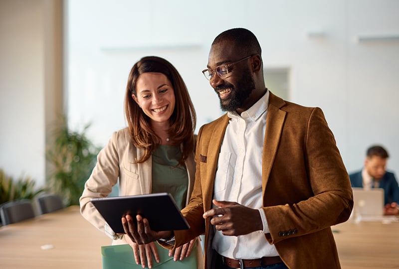 Smiling man and woman interacting with a tablet computer held by the man.