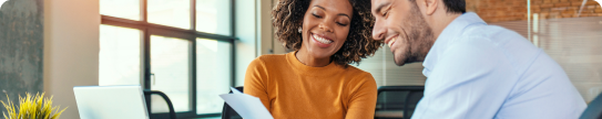 smiling man and woman looking at papers on a desk.