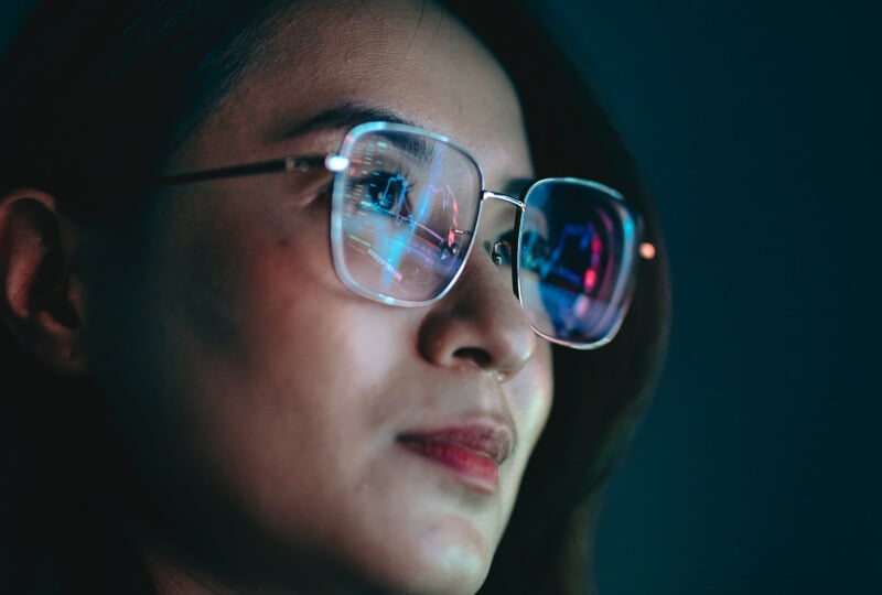 Closeup shot of a woman wearing glasses with computer screens reflected off of the lenses.