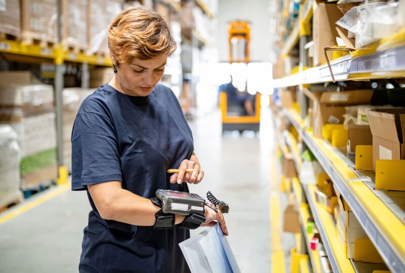 Woman inside a warehouse interacting with a wrist-mounted device.