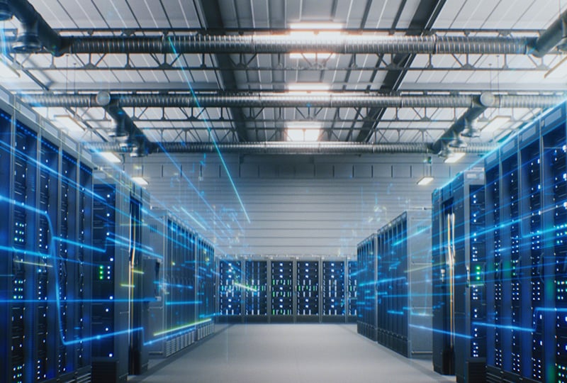 A modern data center with rows of server racks and visible cooling ducts overhead. Blue digital lines and glowing elements overlay the image, representing data flow and network activity within the facility.