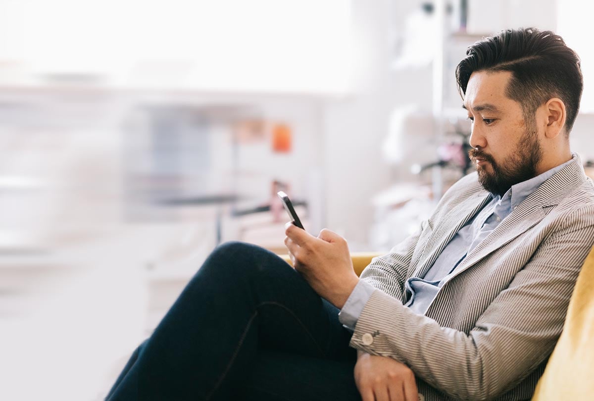 side angle photo of man scrolling on phone with legs crossed