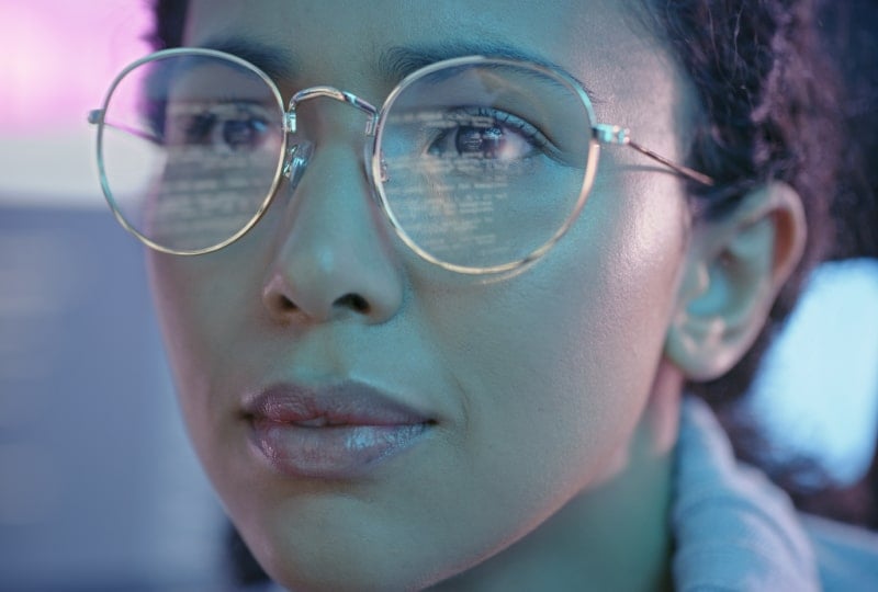 A woman's face with a computer screen reflecting in her glasses
