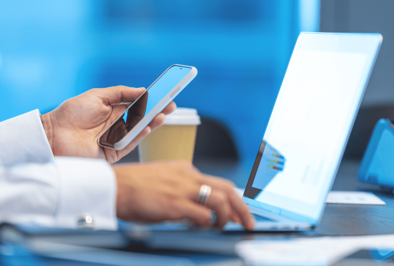 Person holding a phone and interacting with a laptop.
