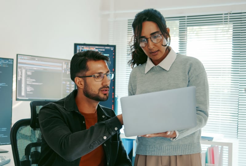 A man and a woman interacting with a laptop held in the woman's hand.