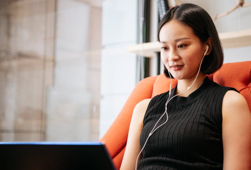 Woman wearing earphones and looking at a laptop screen.