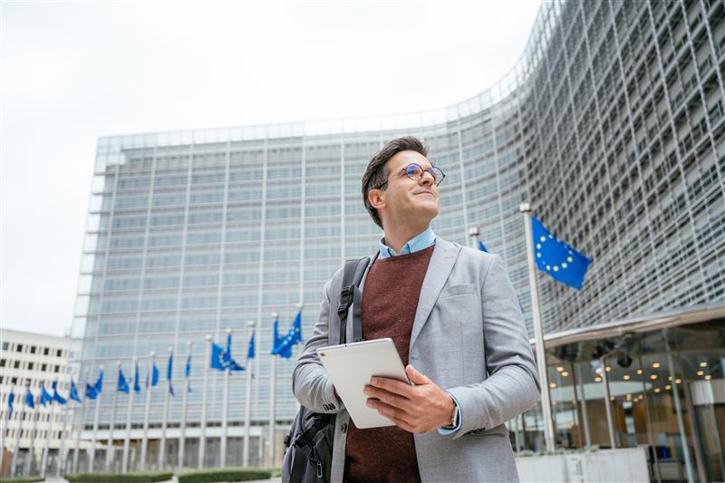 a man holding a tablet device standing infront of the european parliament