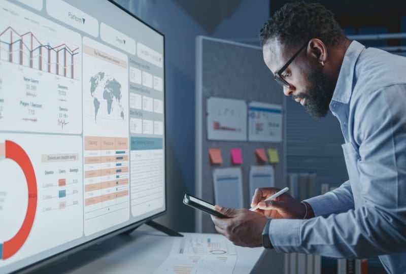a man standing infront of a monitor is taking notes on a handheld device