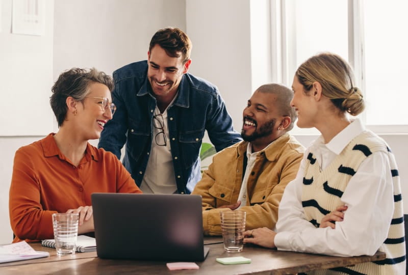 a group of people discussing in.a conference room while looking at a laptop monitor