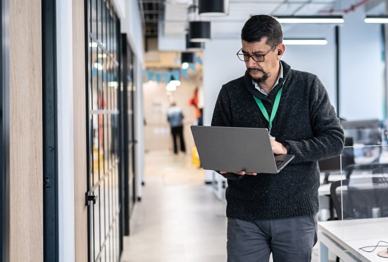 Man walking through an office space while interacting with his laptop.