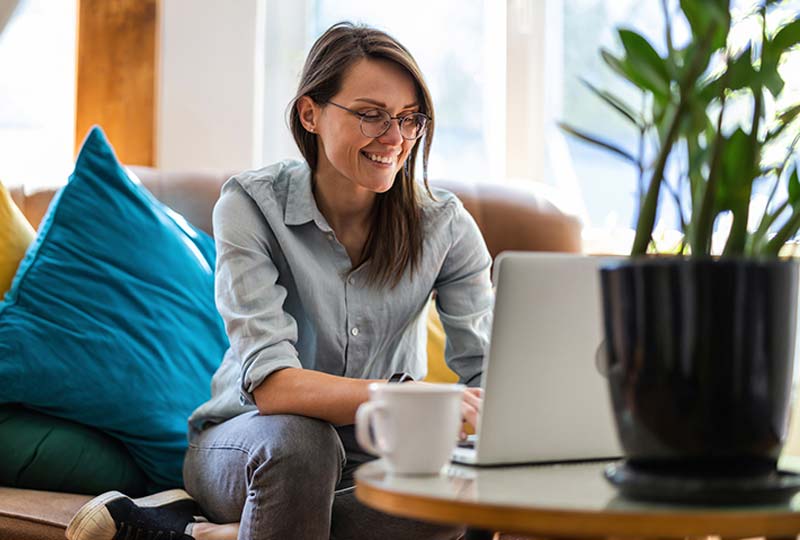 A smiling woman sitting on a couch using a laptop.