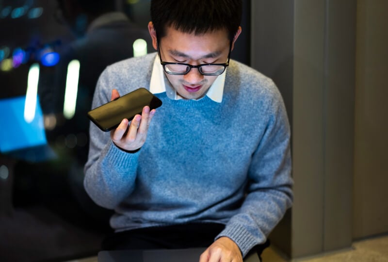 A man wearing glasses engrossed in a conversion on his mobile device.