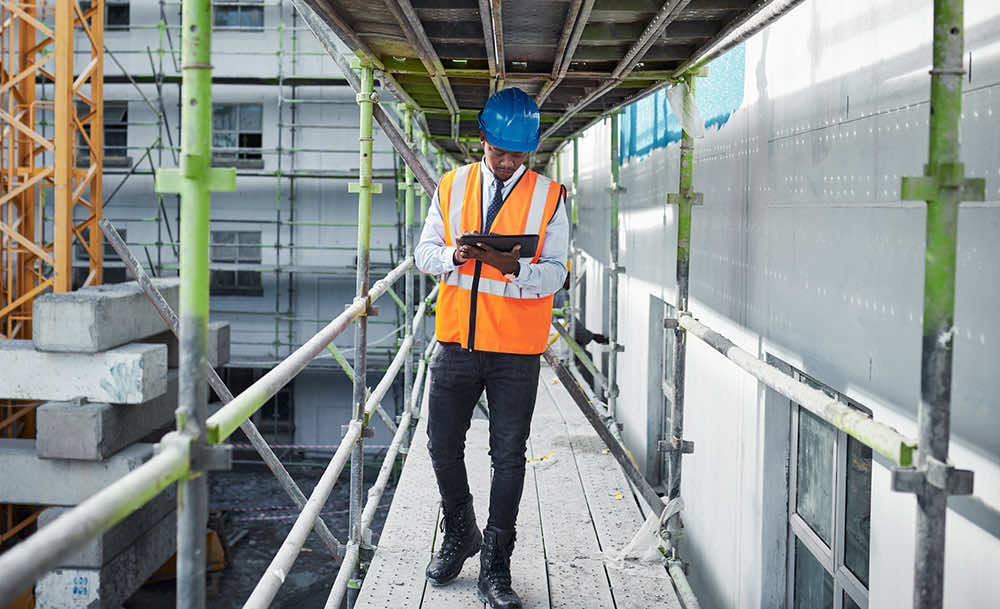 hard-hat worker walking on site while looking at ipad