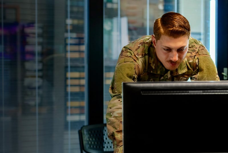 Man dressed in military fatigues working at a desktop computer